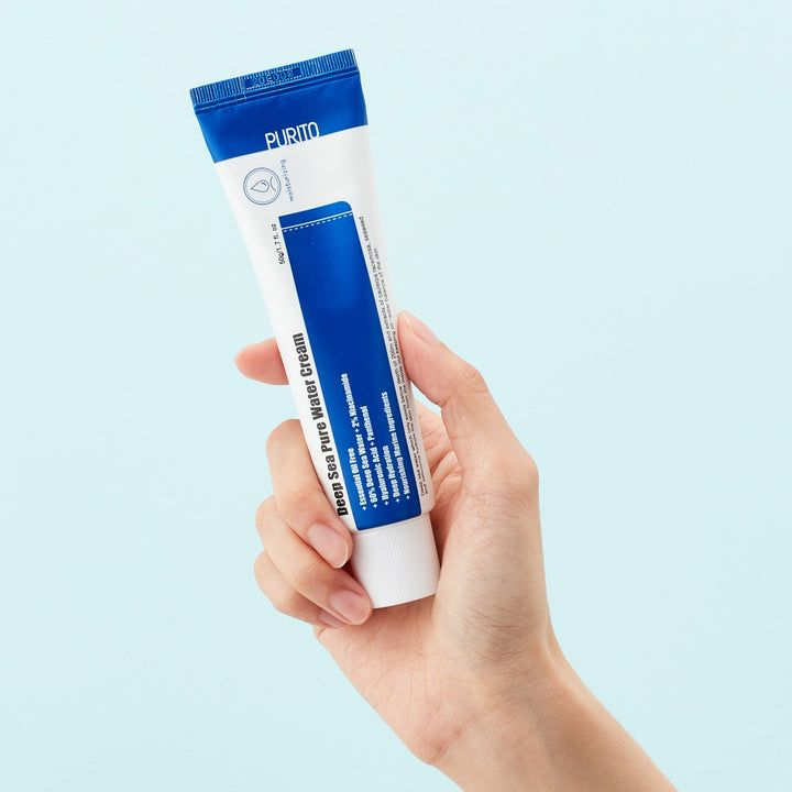 Mano che tiene un tubo di crema. Tubo blu e bianco. Testo: Deep Sea Pure Water Cream. Marchio PURITO. Sfondo azzurro.