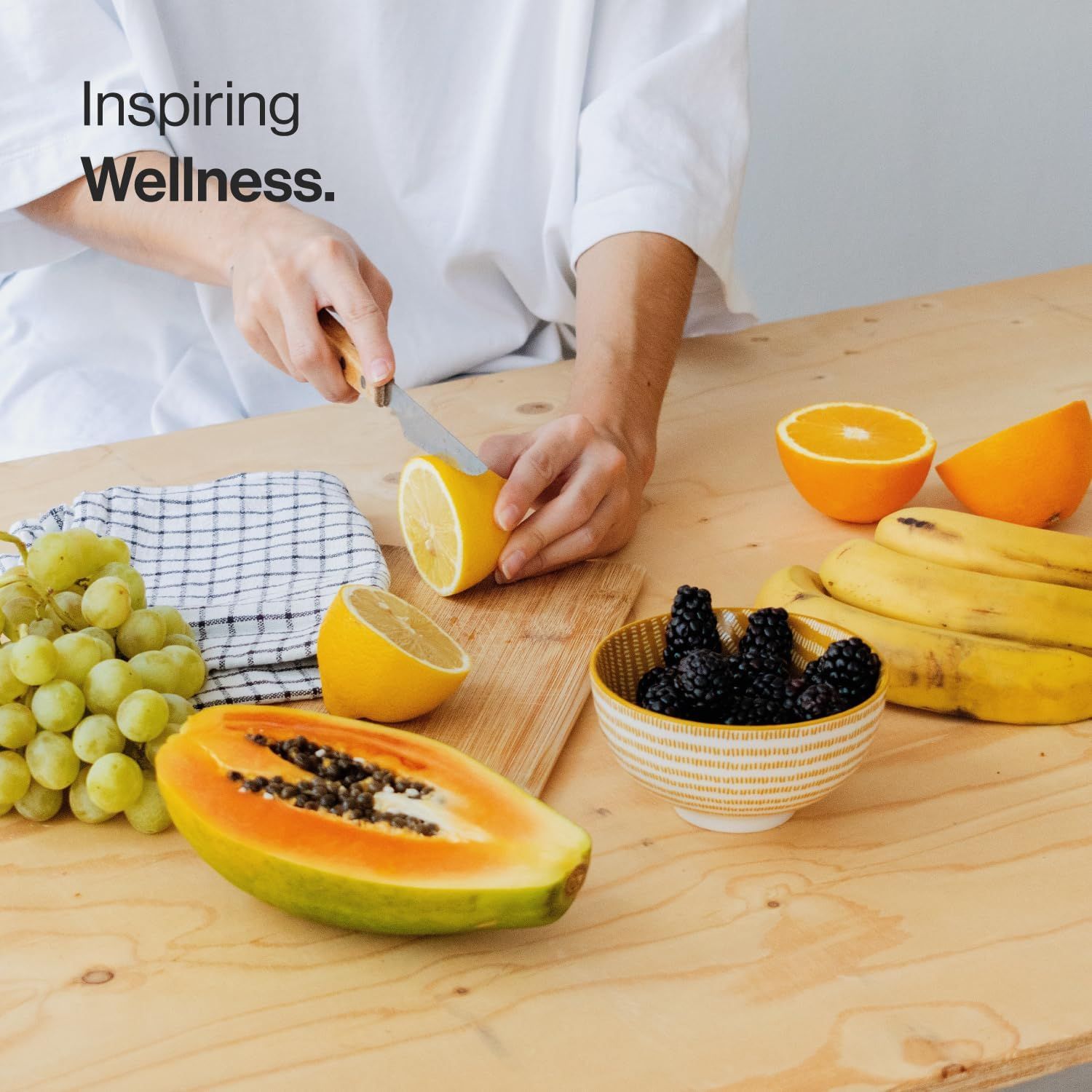 Persona che taglia un limone su un tagliere di legno. Sul tavolo: frutta, tra cui banane, more e papaya.