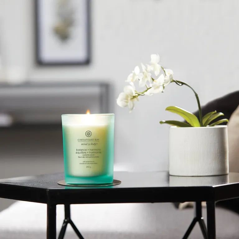 Candela verde accesa su tavolo. Scritta: Chesapeake Bay, balance + harmony. Accanto a orchidea in vaso.