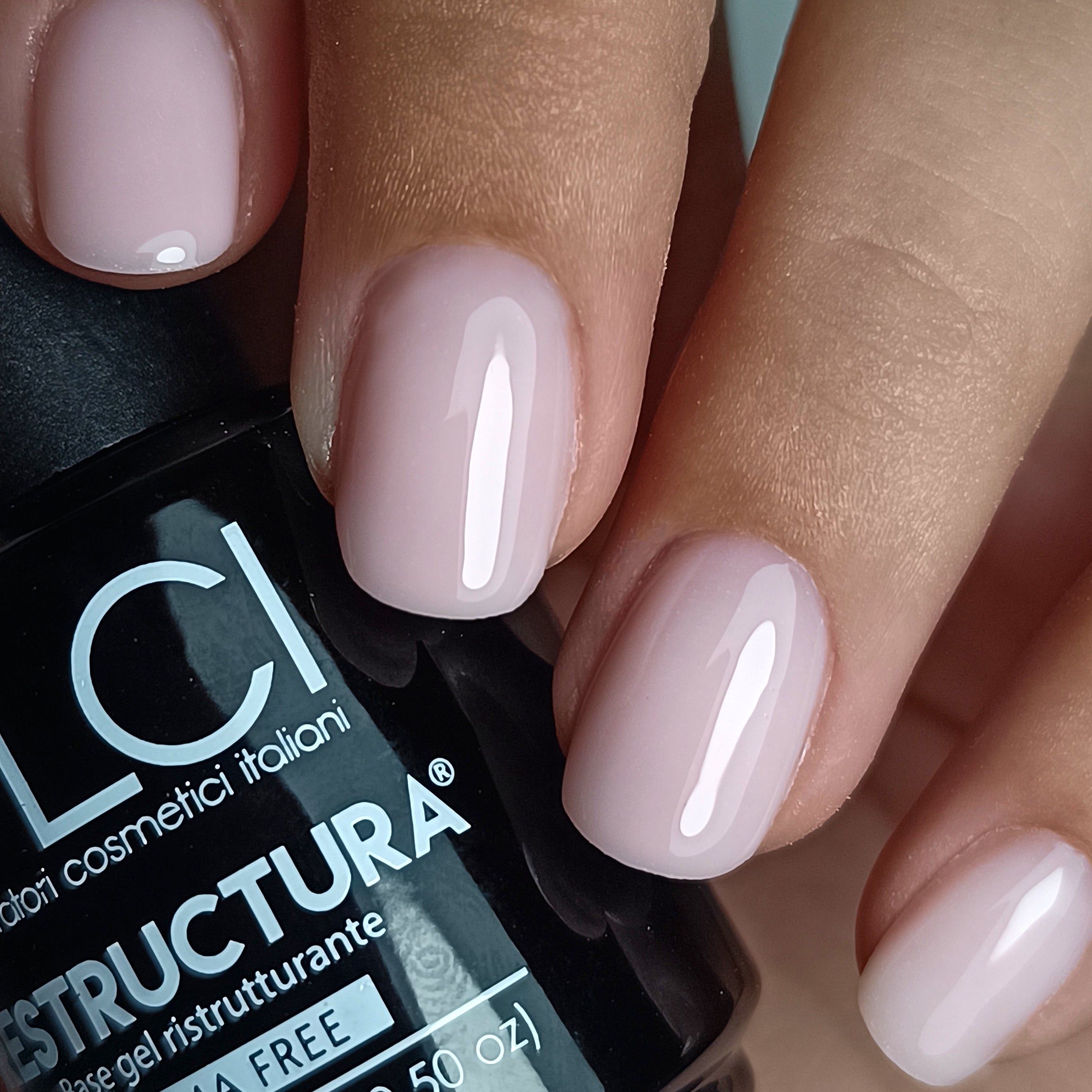 Mano con unghie smaltate rosa chiaro. Flacone con scritta LCI Restructura Base gel ristrutturante Hema Free.