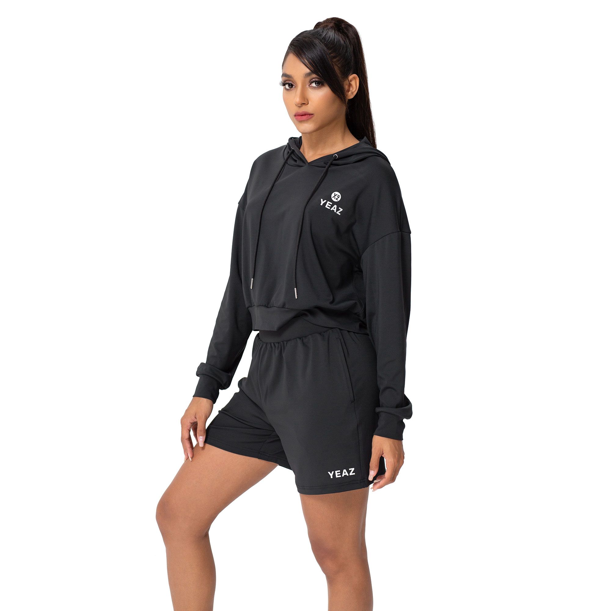 Completo athleisure nero: felpa corta con cappuccio e coulisse e pantaloncini coordinati. Entrambi con logo bianco.