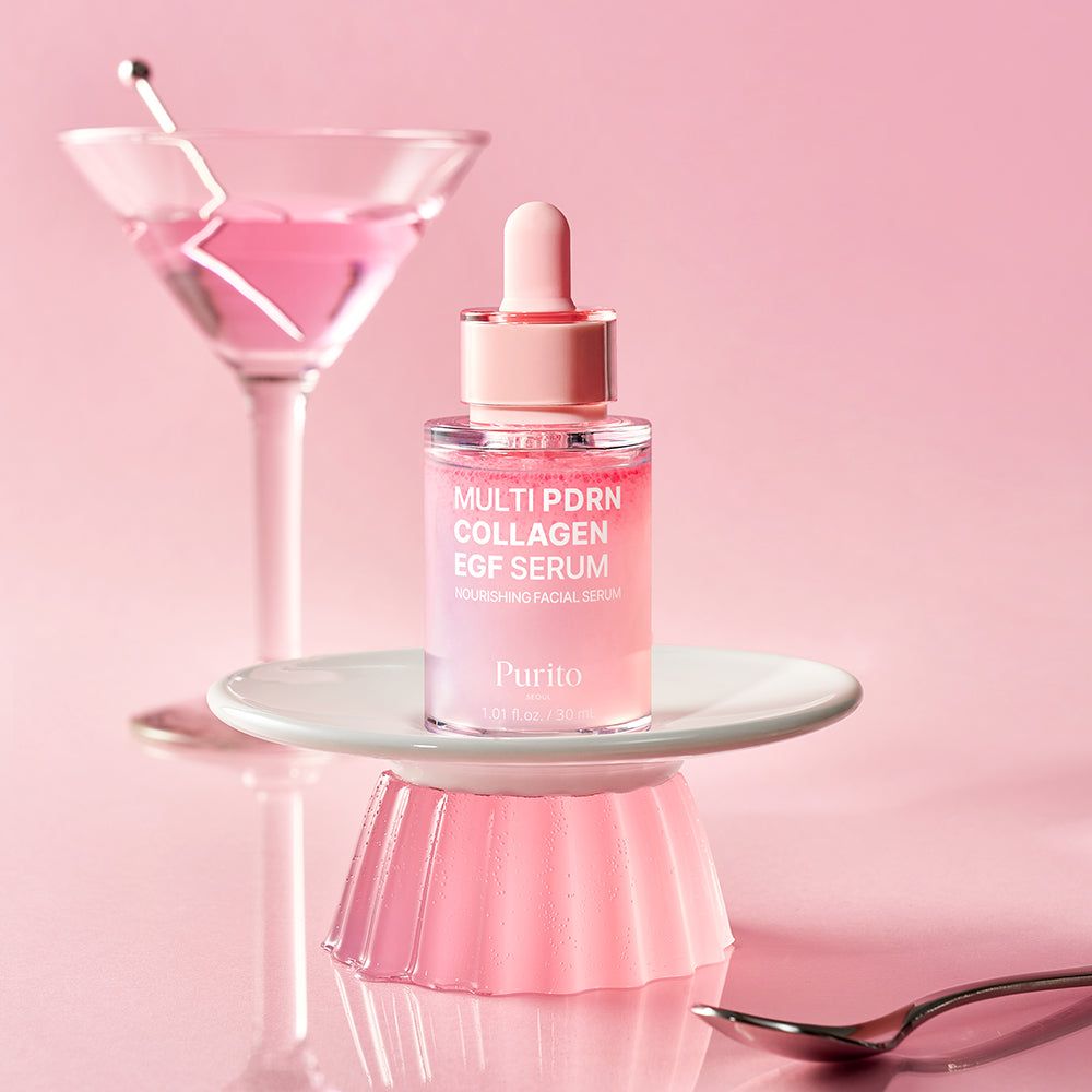 Flacone di siero PURITO su un piatto accanto a un bicchiere da martini con liquido rosa.