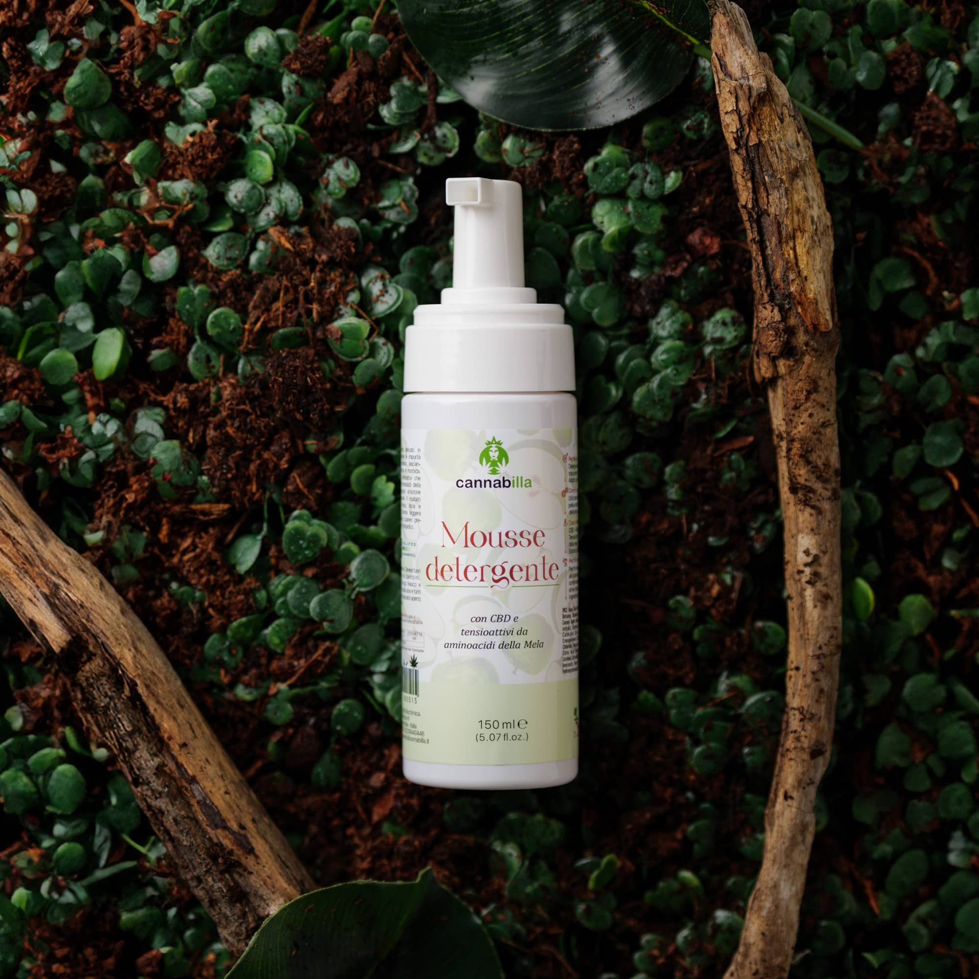 Flacone bianco con erogatore, Cannabilla Mousse detergente, su sfondo verde con rami. Contiene CBD e acido malico. 150 ml.