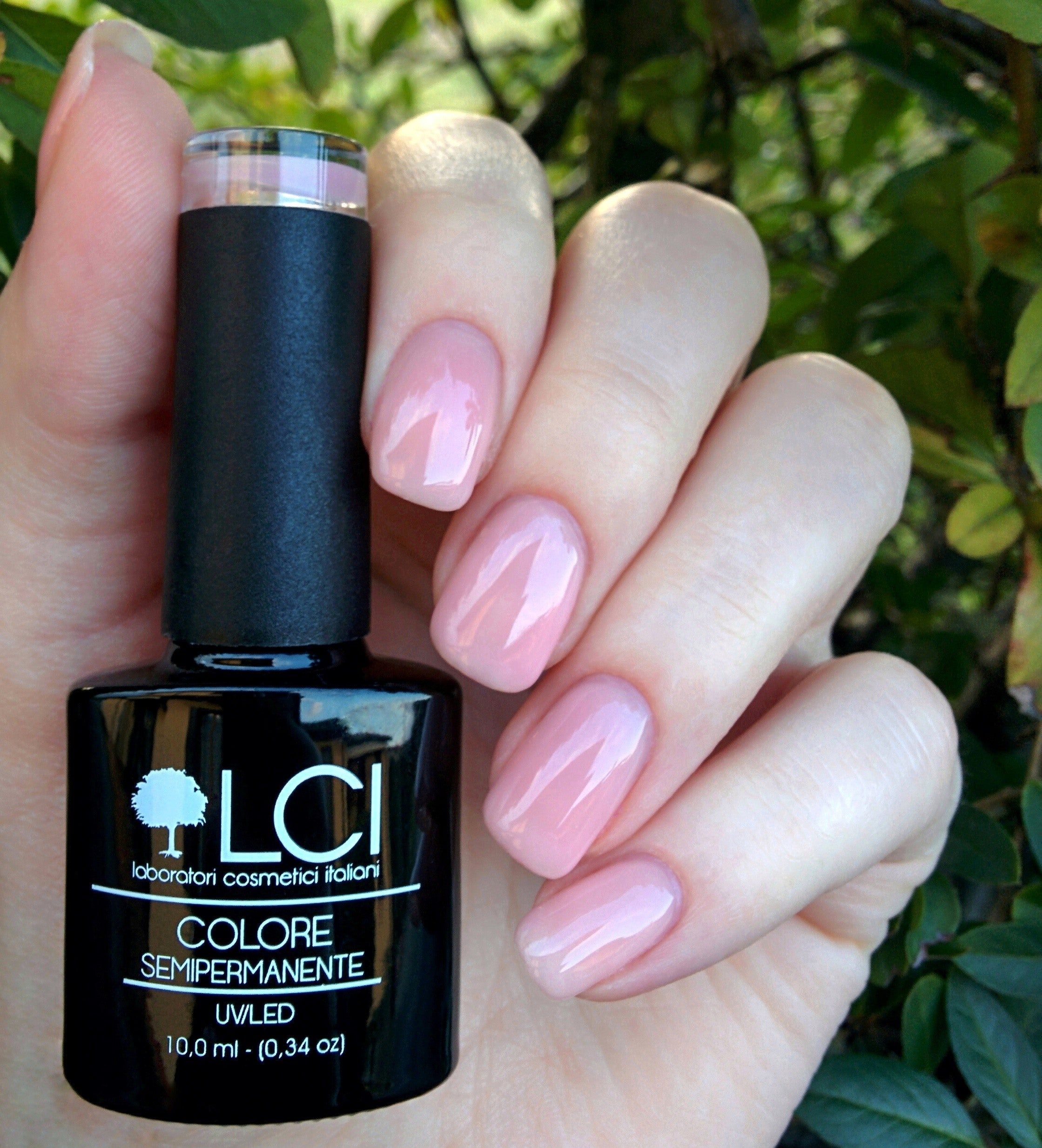 Mano con unghie smaltate e flacone di smalto. Smalto semipermanente rosa. Flacone nero, testo bianco. Logo LCI.