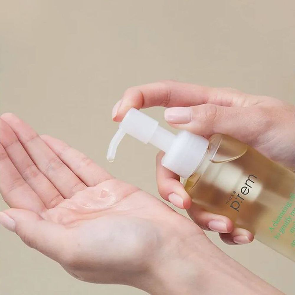 Mani che tengono una bottiglia trasparente con pompa. L'olio viene versato nel palmo. Scritta: prem.