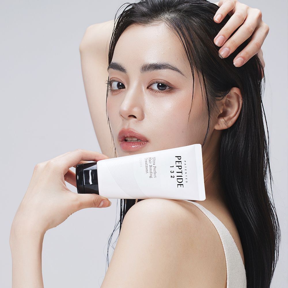 Una donna tiene un tubo bianco con scritta PEPTIDE 132 Ultra Perfect Hair Bonding Treatment.