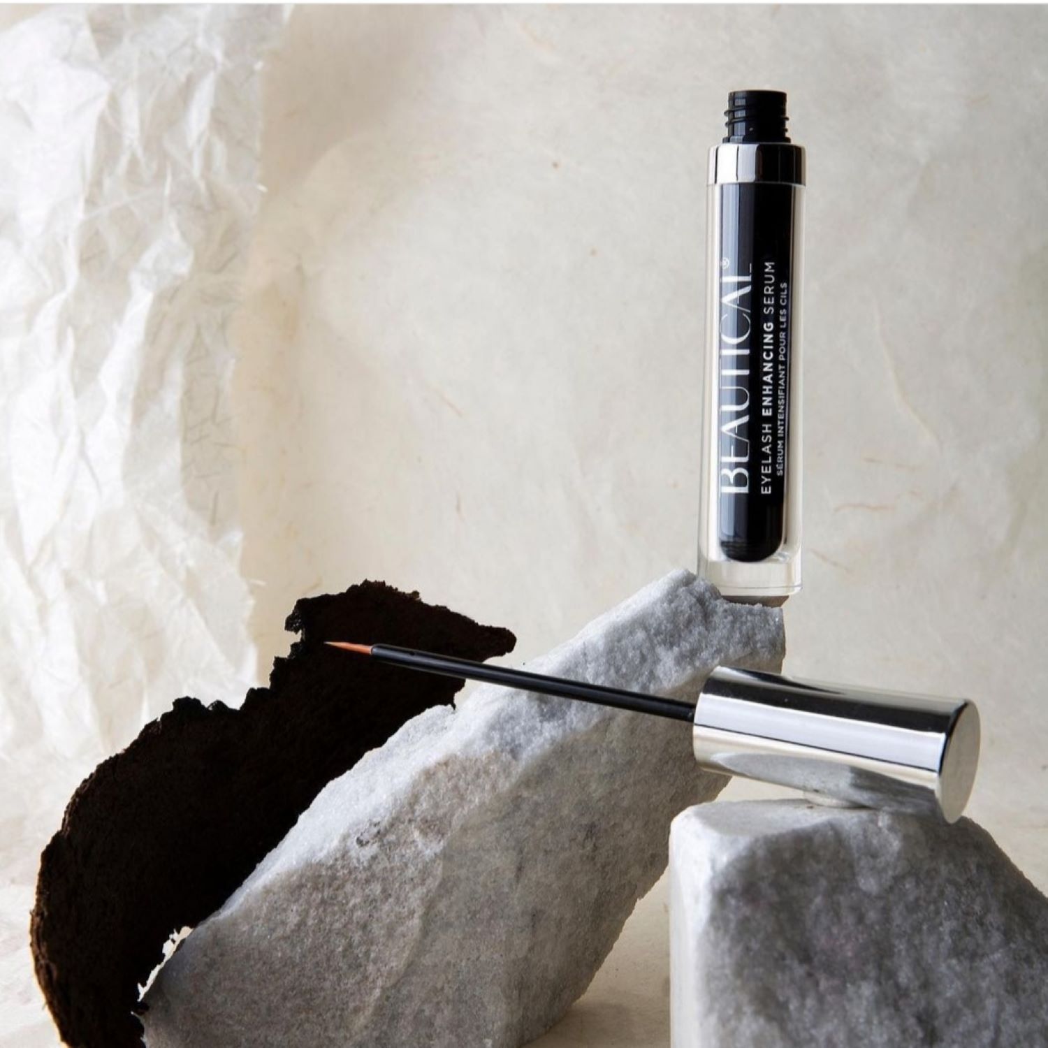 Siero per ciglia Beautical. Flacone nero, tappo argentato, applicatore. Su pietra.