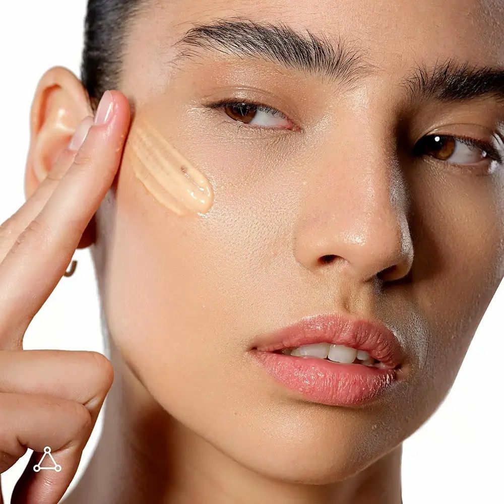 Primo piano di una donna che applica un prodotto sulla guancia. Il prodotto è marrone chiaro e applicato con il dito.