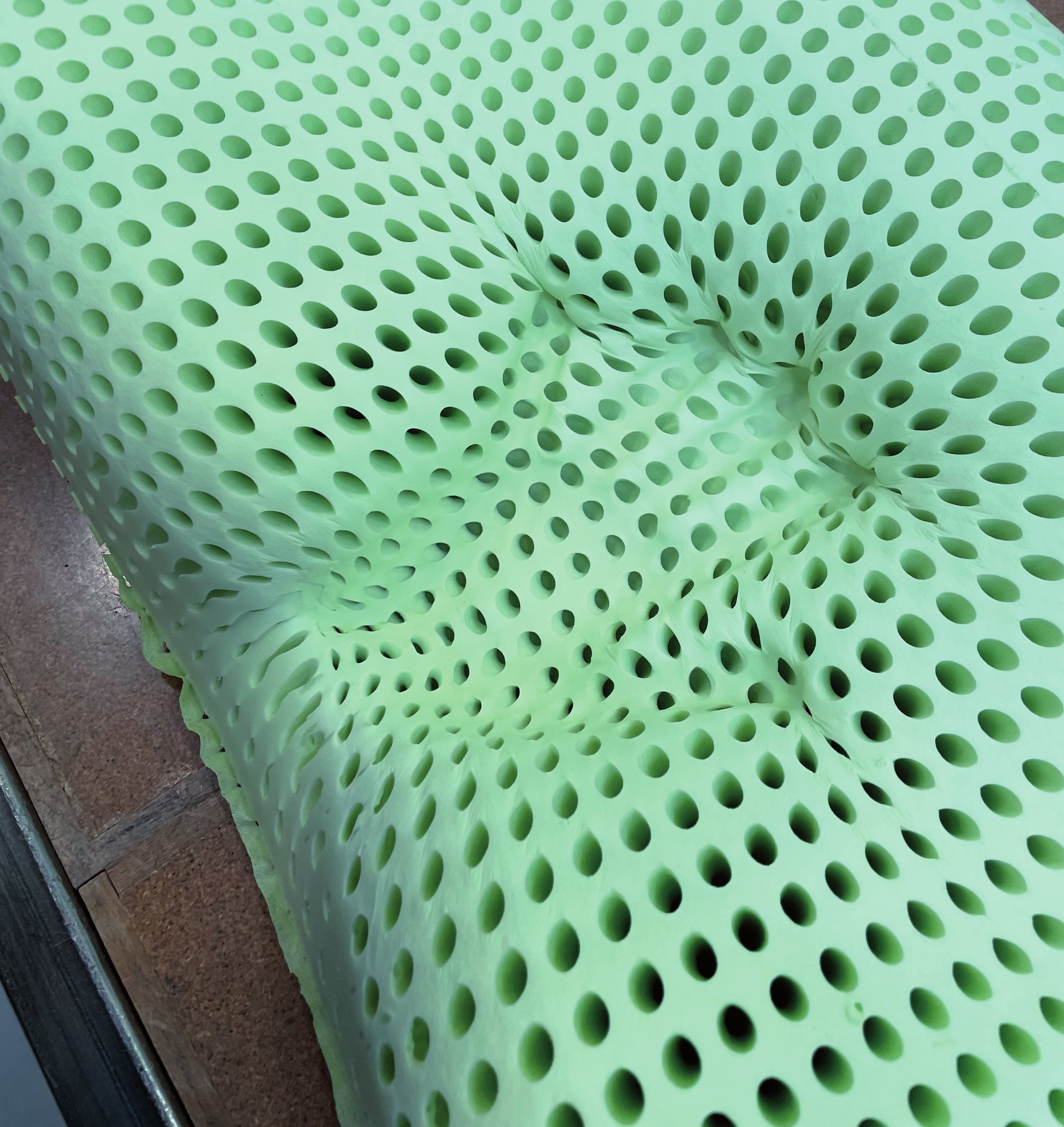 Cuscino verde chiaro con numerosi fori. Superficie irregolare con una rientranza.