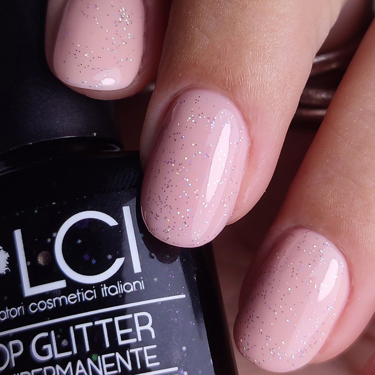 Smalto rosa glitterato sulle unghie. Flacone con nome del prodotto sullo sfondo.