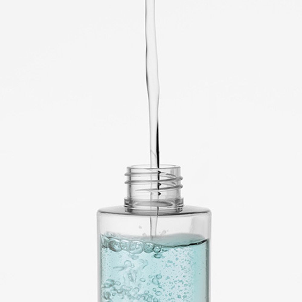 Primo piano di una bottiglia che versa liquido. La bottiglia è trasparente con contenuto blu. Il tappo è aperto.