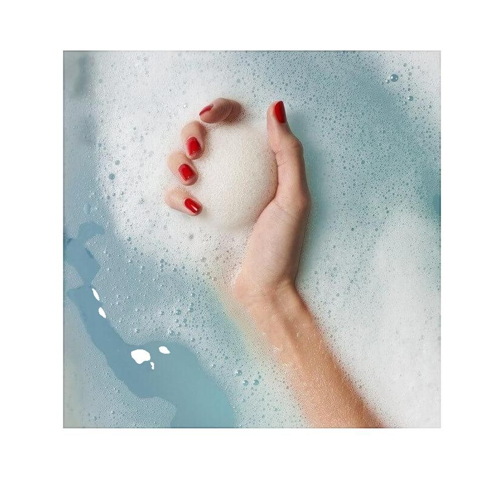 Mano che tiene una spugna Konjac in acqua saponata. Unghie rosse. Acqua blu e schiumosa.