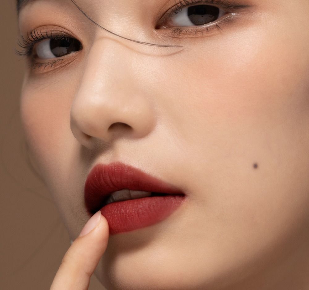 Primo piano di una persona con rossetto rosso scuro. Un dito tocca le labbra.