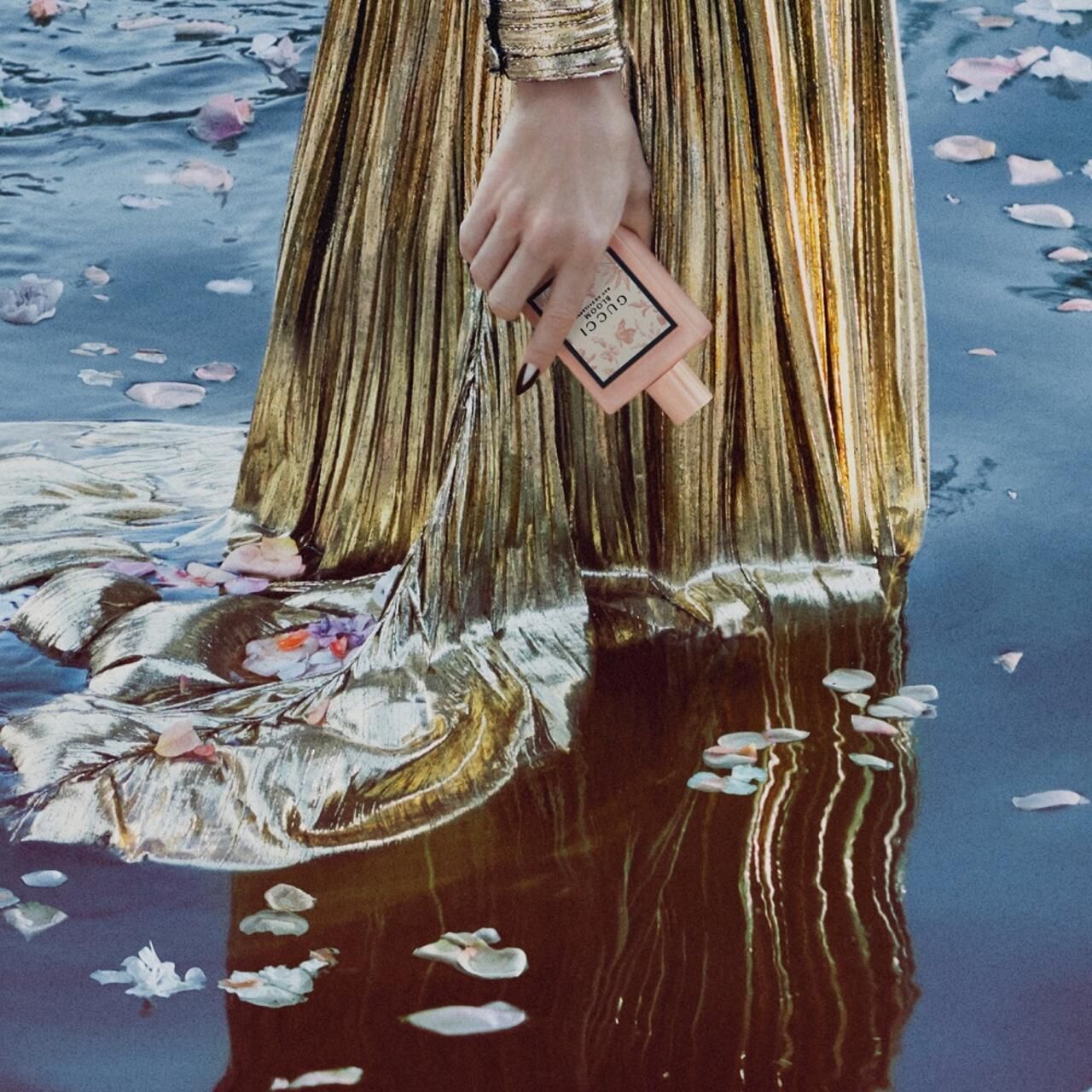 Mano che tiene un flacone rosa con stampa floreale nell'acqua. Scritta: Gucci Bloom Eau de Toilette.
