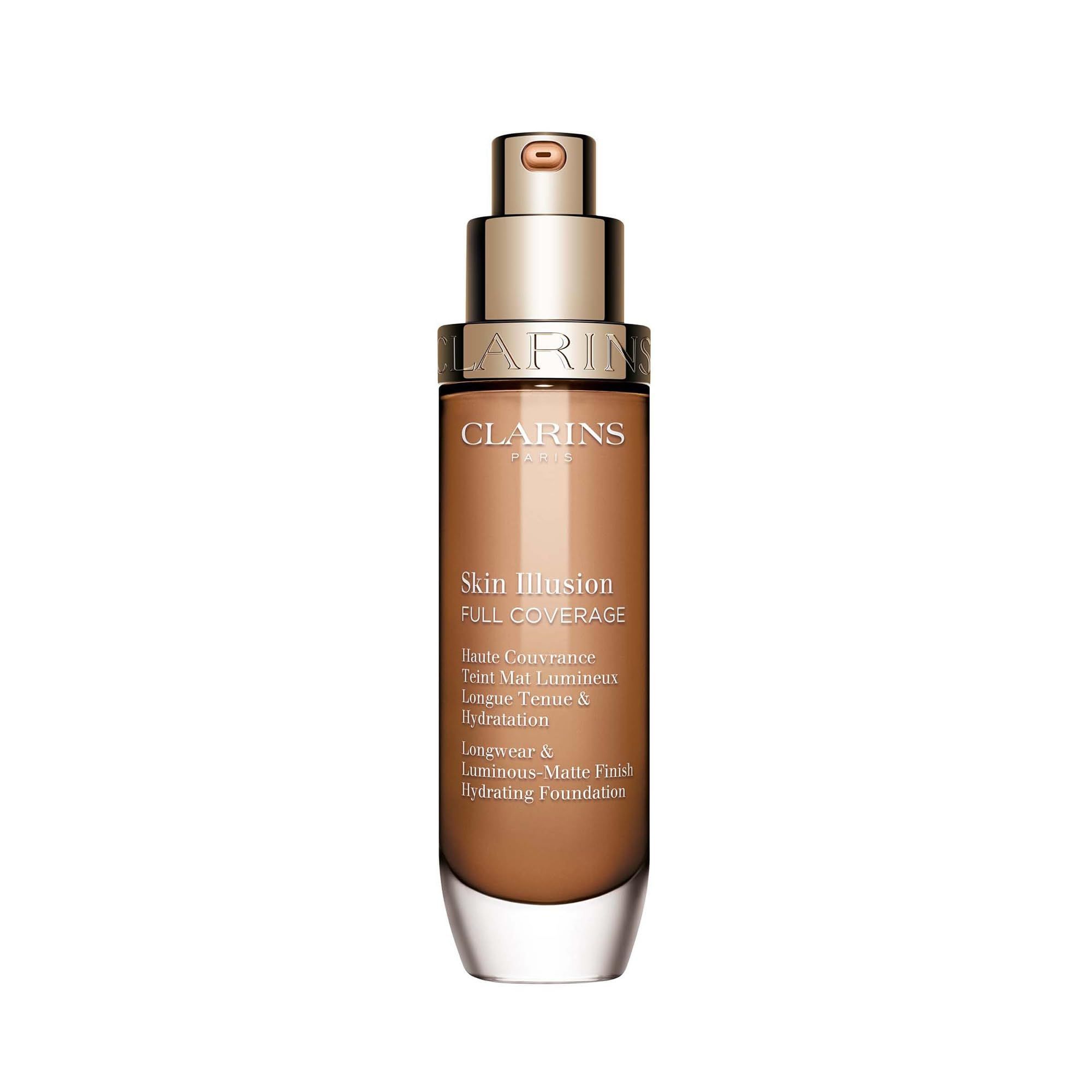 Flacone di fondotinta marrone con tappo dorato. Scritta: Skin Illusion Full Coverage. Marchio: Clarins.
