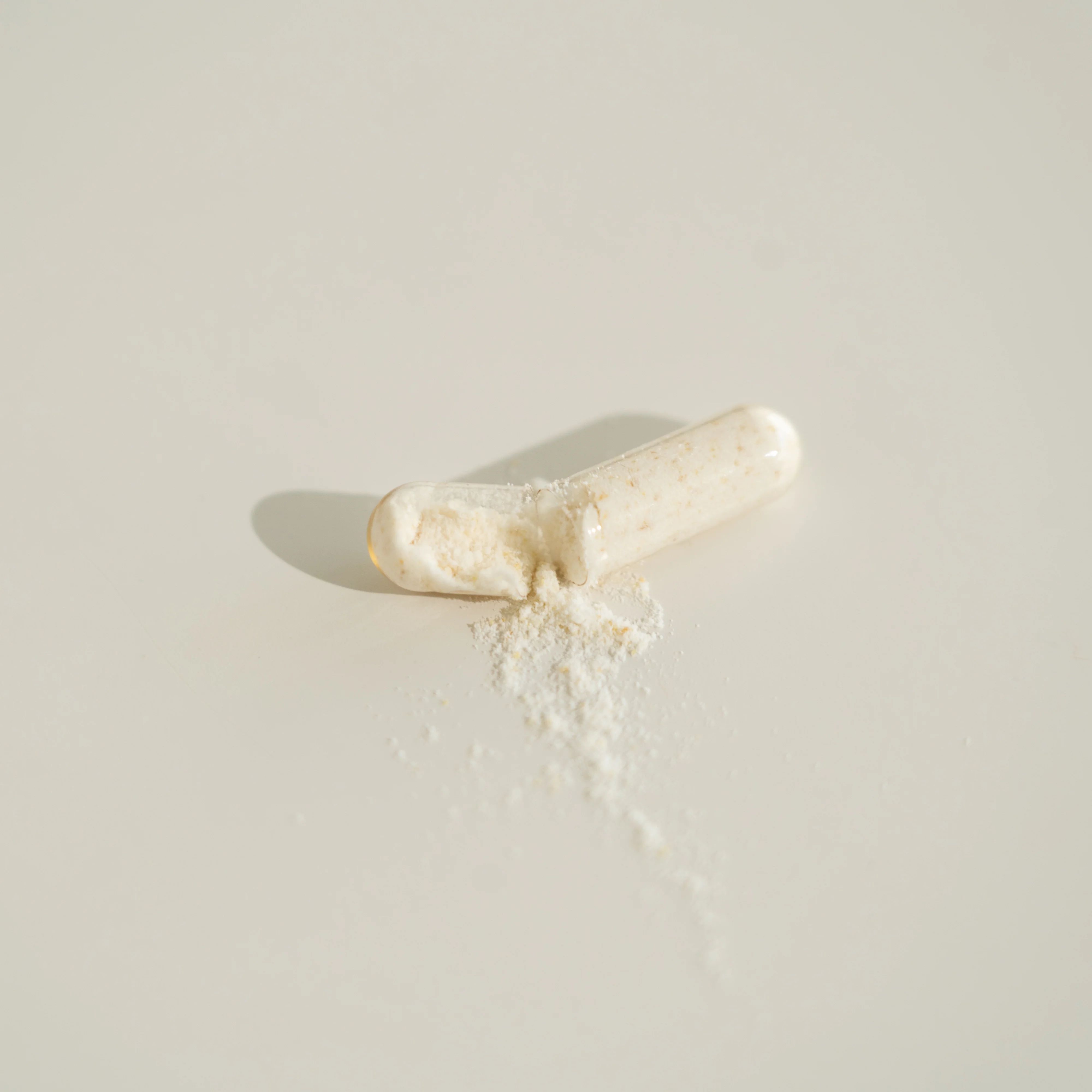Capsula bianca aperta con contenuto in polvere su sfondo chiaro.