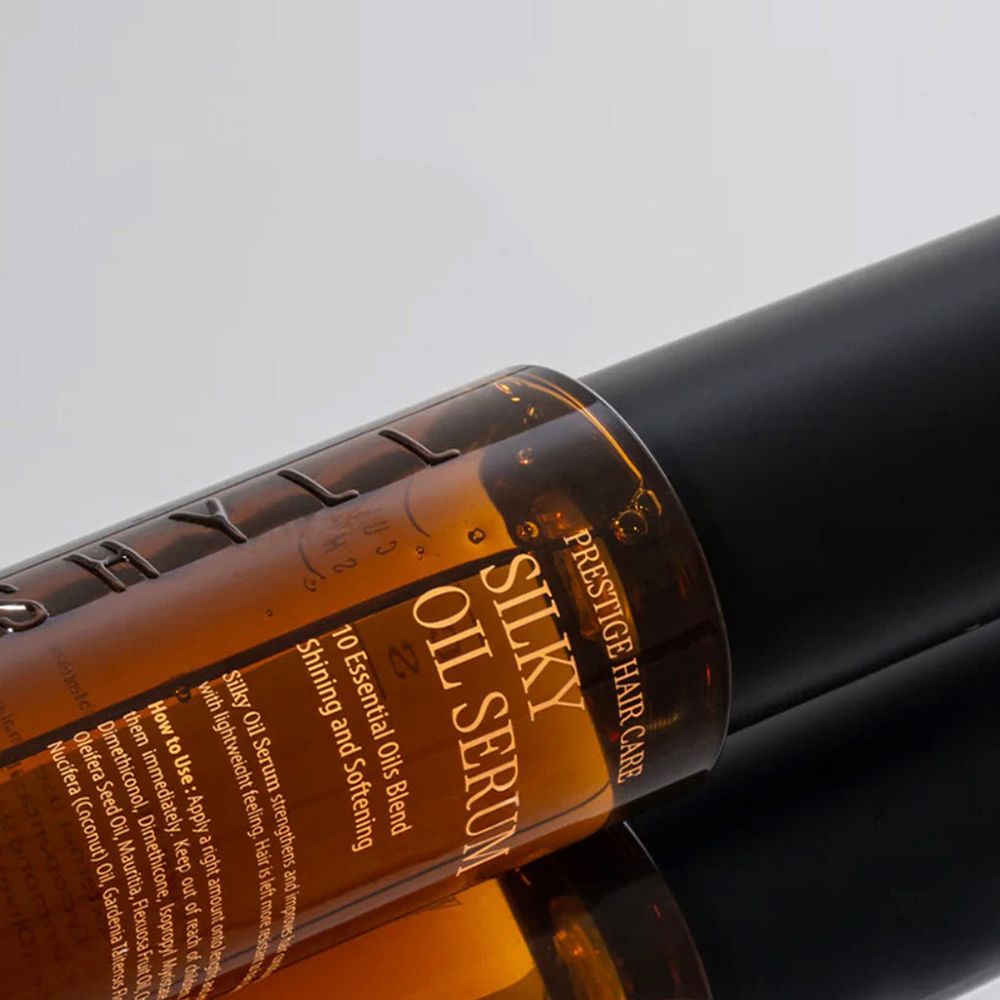 Primo piano di un flacone di olio per capelli marrone con tappo nero. Scritta: Silky Oil Serum. Testo: 10 Essential Oils Blend. Per cura pro.