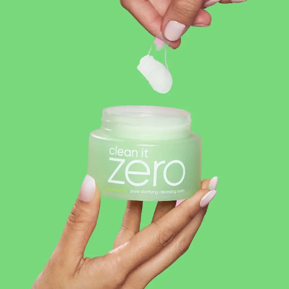 Vasetto verde con coperchio bianco. Nome prodotto "clean it zero" e "pore clarifying cleansing balm" visibili. Mani che tengono il prodotto e la massa.