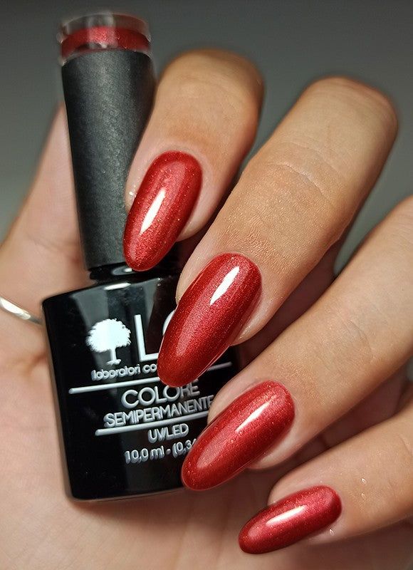 Mano con unghie smaltate e flacone di smalto. Smalto rosso glitterato. Logo LCI visibile.