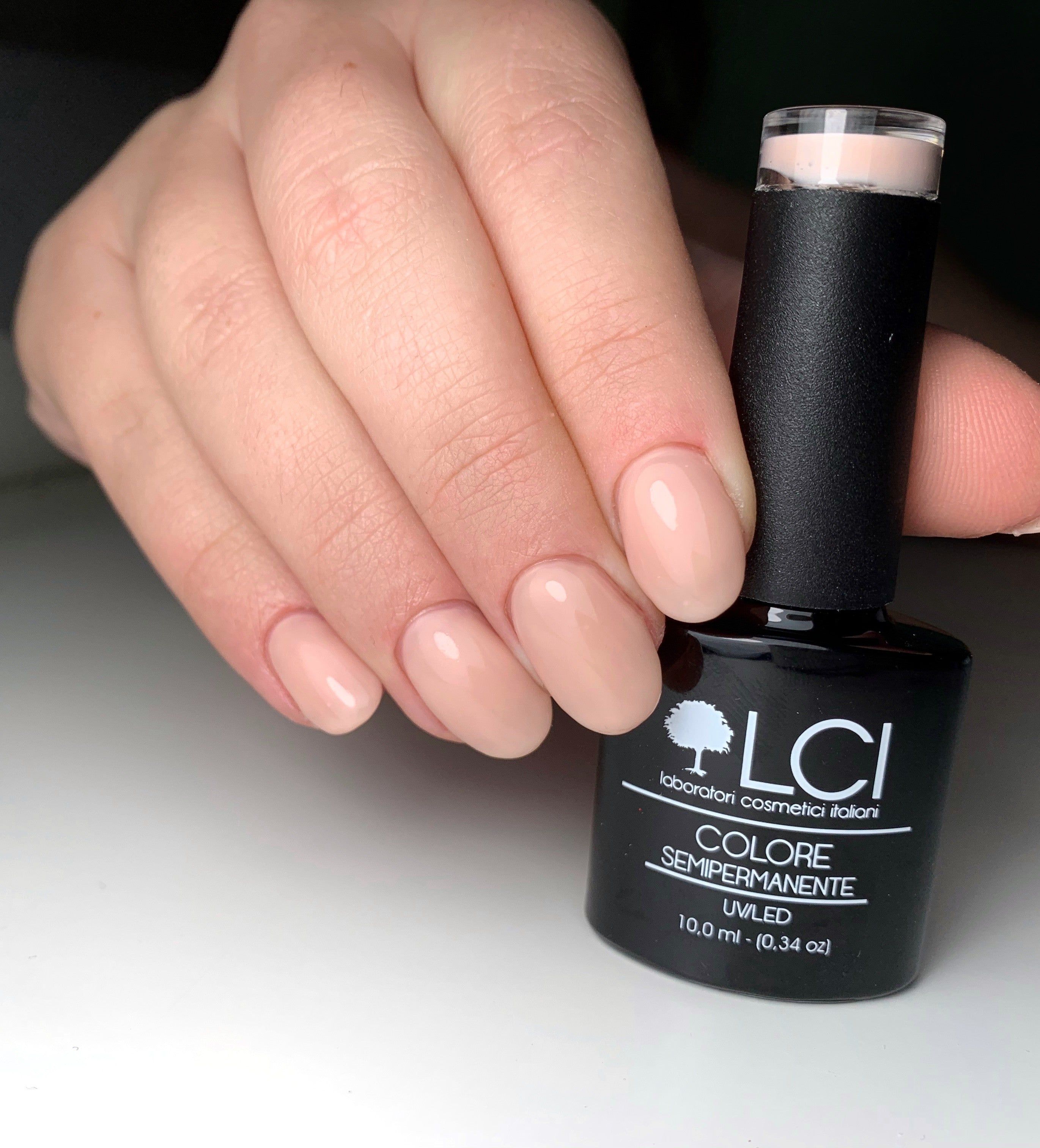 Mano con unghie smaltate rosa nude. Flacone di smalto accanto. Marchio LCI Cosmetics.