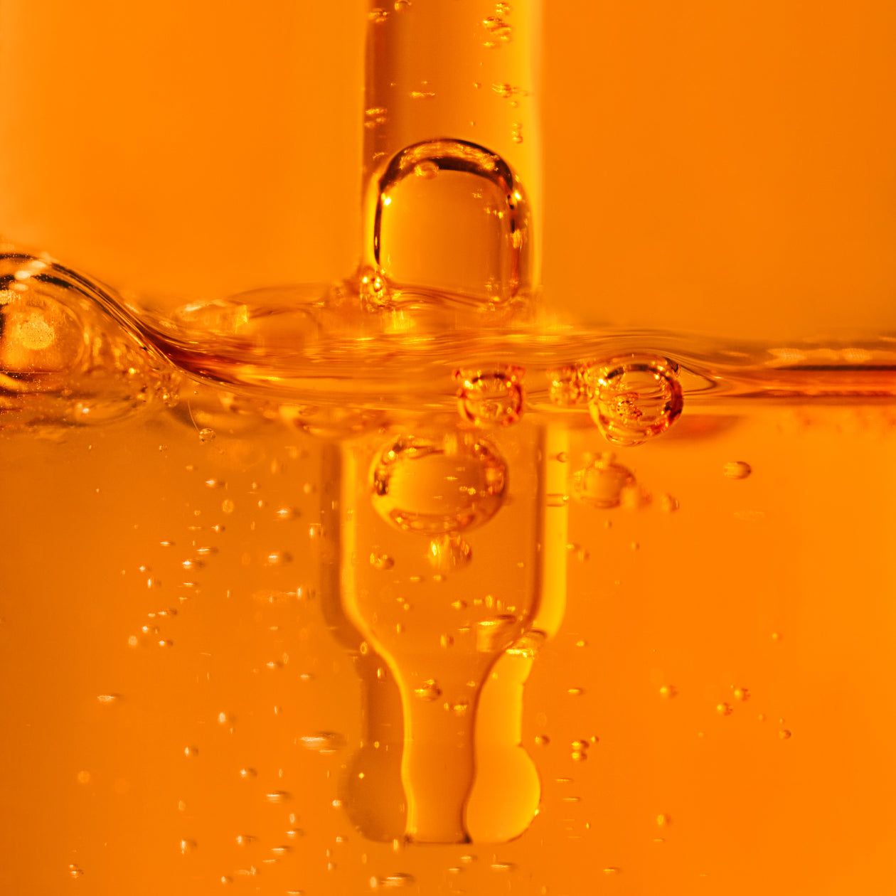 Primo piano di una pipetta in un liquido arancione. Bolle visibili.