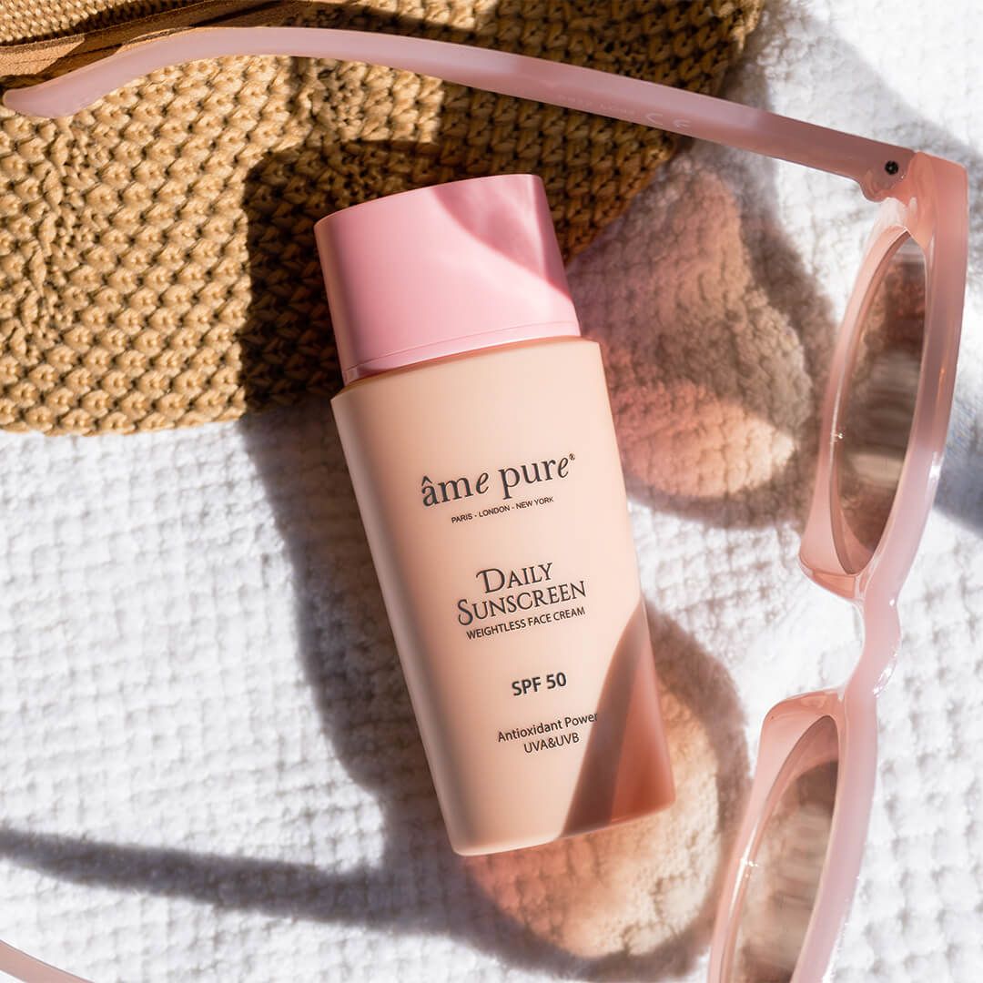 Flacone Âme Pure Daily Sunscreen accanto a occhiali da sole e borsa, SPF 50.