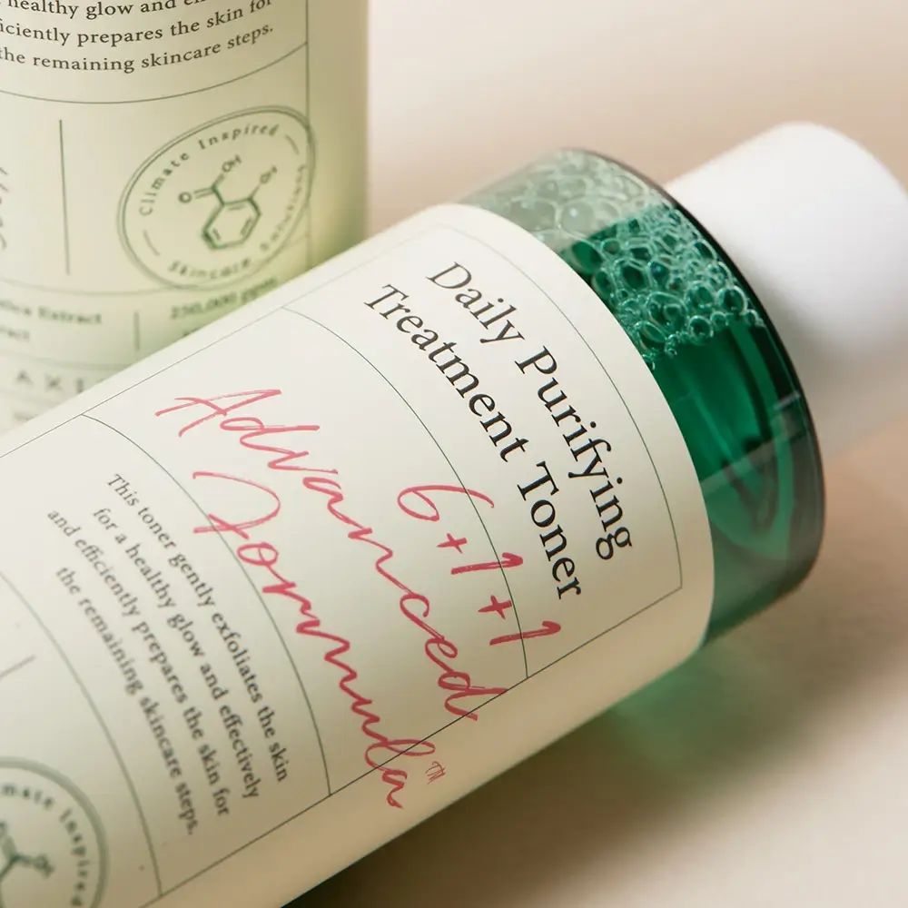 Primo piano di un flacone di toner. Scritta: Daily Purifying Treatment Toner. Liquido verde visibile.