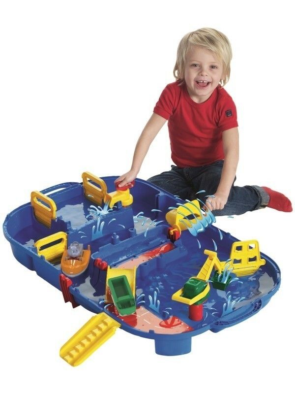 Giocattolo blu con vasca d'acqua, elementi gialli e barche. Un bambino è seduto davanti.