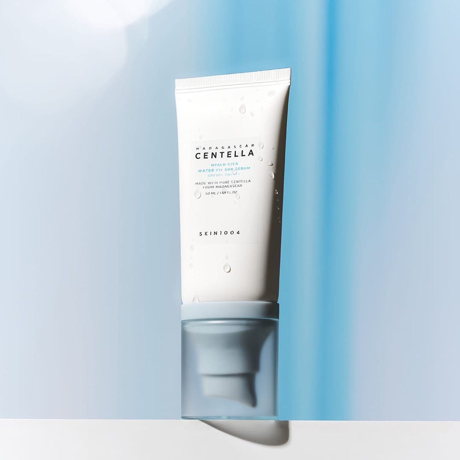 SKIN1004 Hyalu-Cica Water-Fit Siero Solare SPF 50+ PA++++ con gocce d'acqua sul tubetto, su sfondo blu.