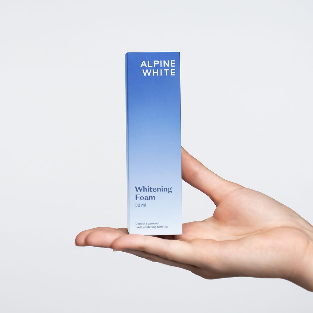 Mano che tiene una scatola con "ALPINE WHITE Whitening Foam". 50 ml.