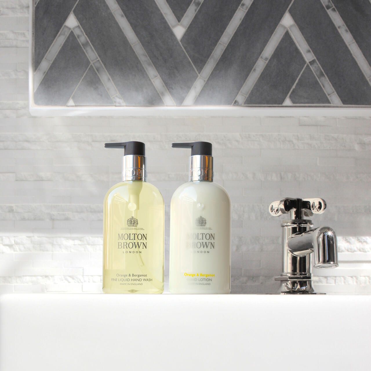 Due flaconi di sapone liquido con dosatore accanto al rubinetto. Scritta: Molton Brown, Orange & Bergamot.