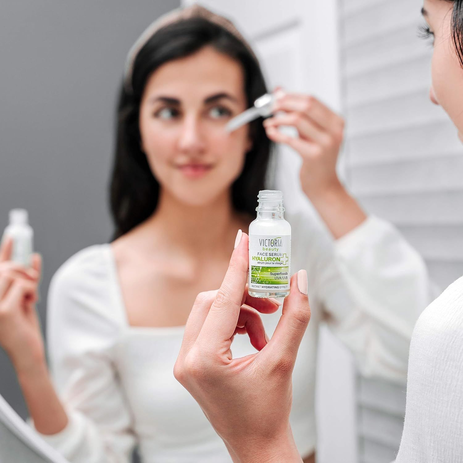 Flacone trasparente con contagocce. Scritta: Victoria Beauty Hyaluron Serum. Persona che tiene flacone e contagocce davanti allo specchio.
