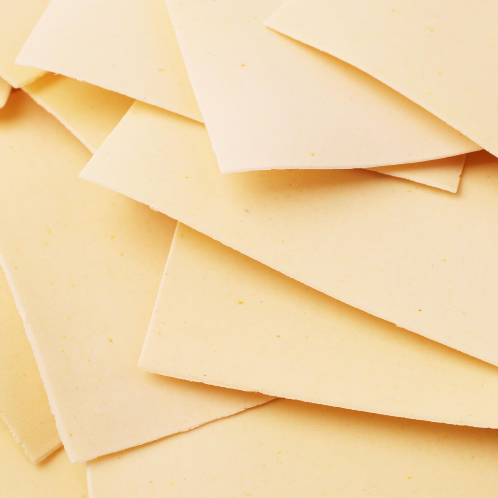 Pila di sfoglie di lasagne non cotte. Forma rettangolare giallo chiaro. Alcune si sovrappongono.