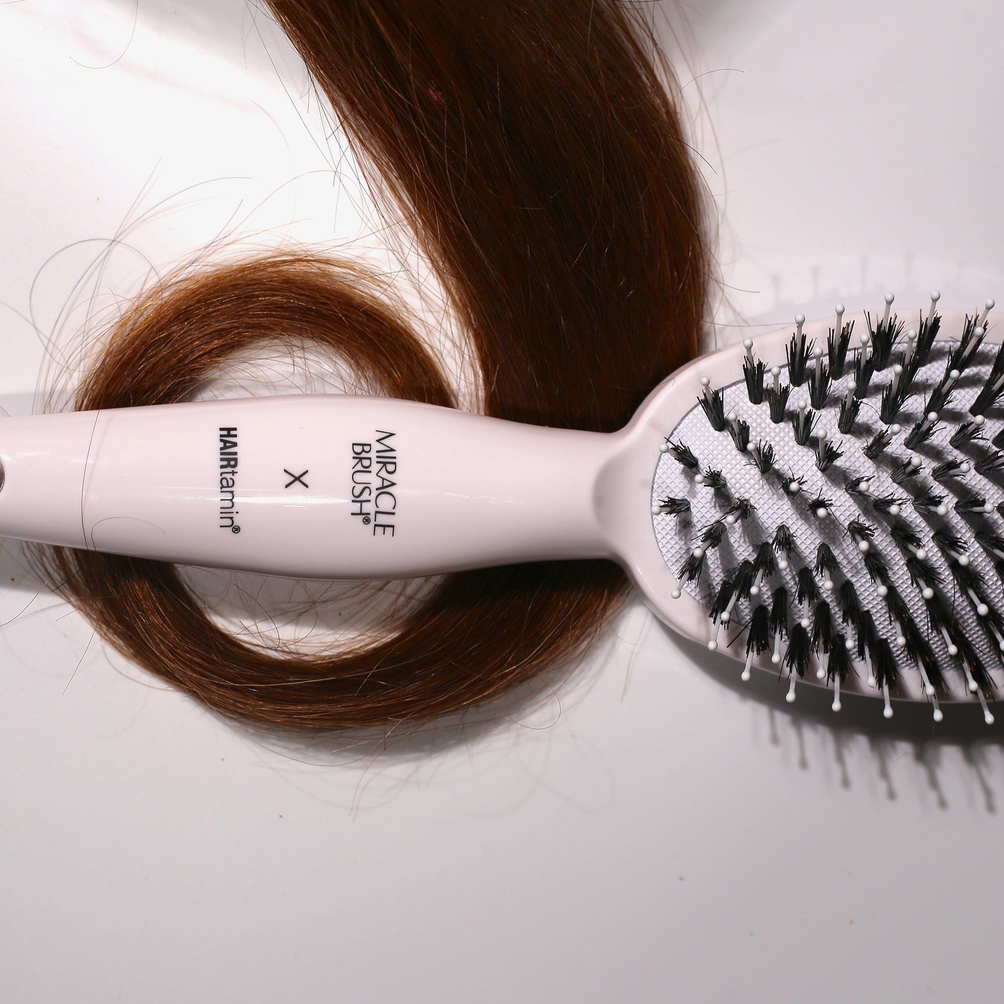 Spazzola bianca con setole nere e una ciocca di capelli. Scritta MIRACLE BRUSH X HAIRtamin.