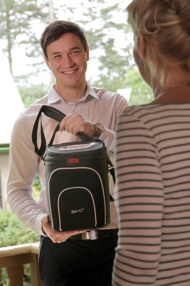 Uomo che tiene il concentratore di ossigeno GCE Zen-O. Borsa nera con tracolla, profilo bianco e logo.