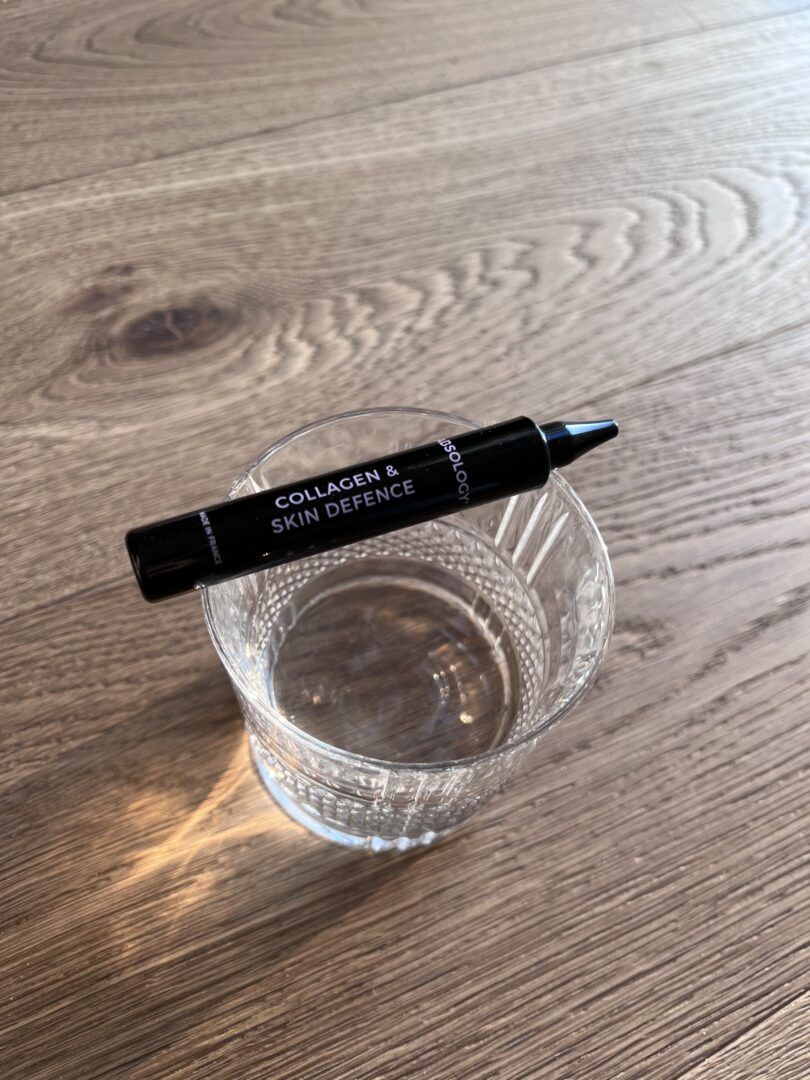 Fiala nera con la scritta "Collagen & Skin Defence" appoggiata su un bicchiere.