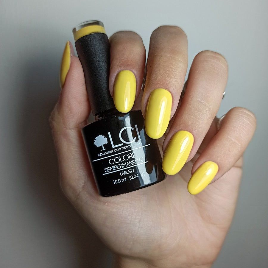 Mano con unghie smaltate e flacone di smalto. Smalto giallo. Scritta: LCI, Colore Semipermanente, UVLED.