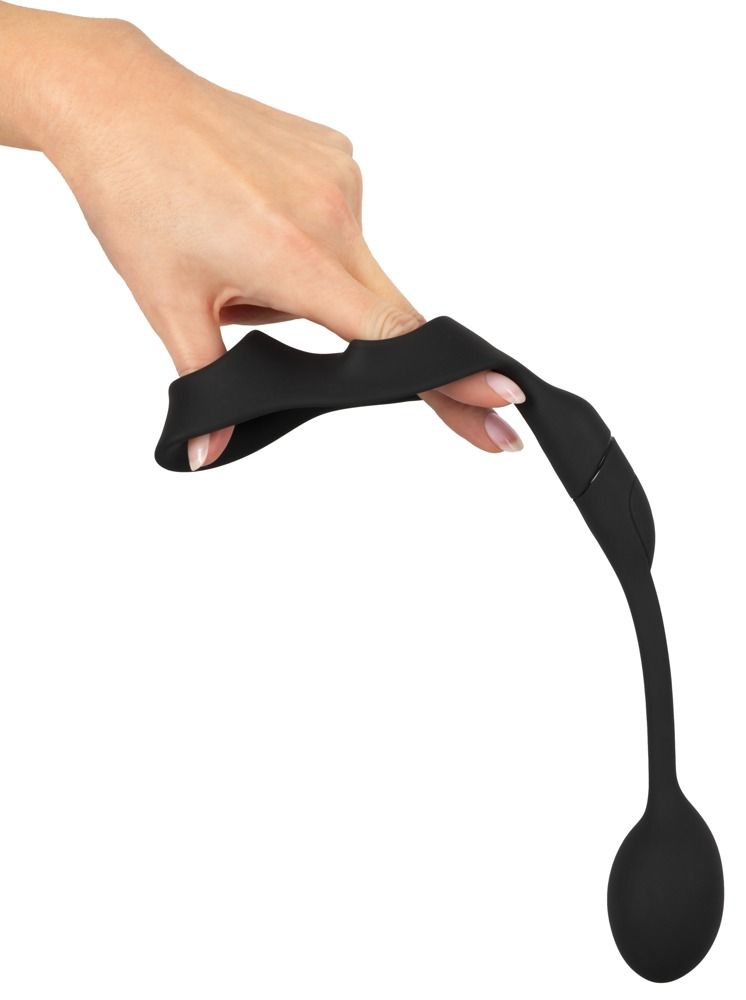 Mano che tiene e piega un anello fallico nero con anello scrotale e plug anale. Materiale flessibile.