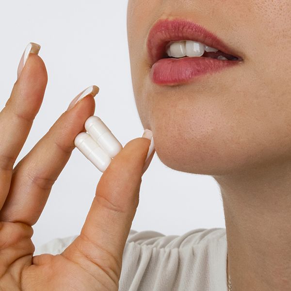 Una donna tiene due capsule bianche tra pollice e indice.