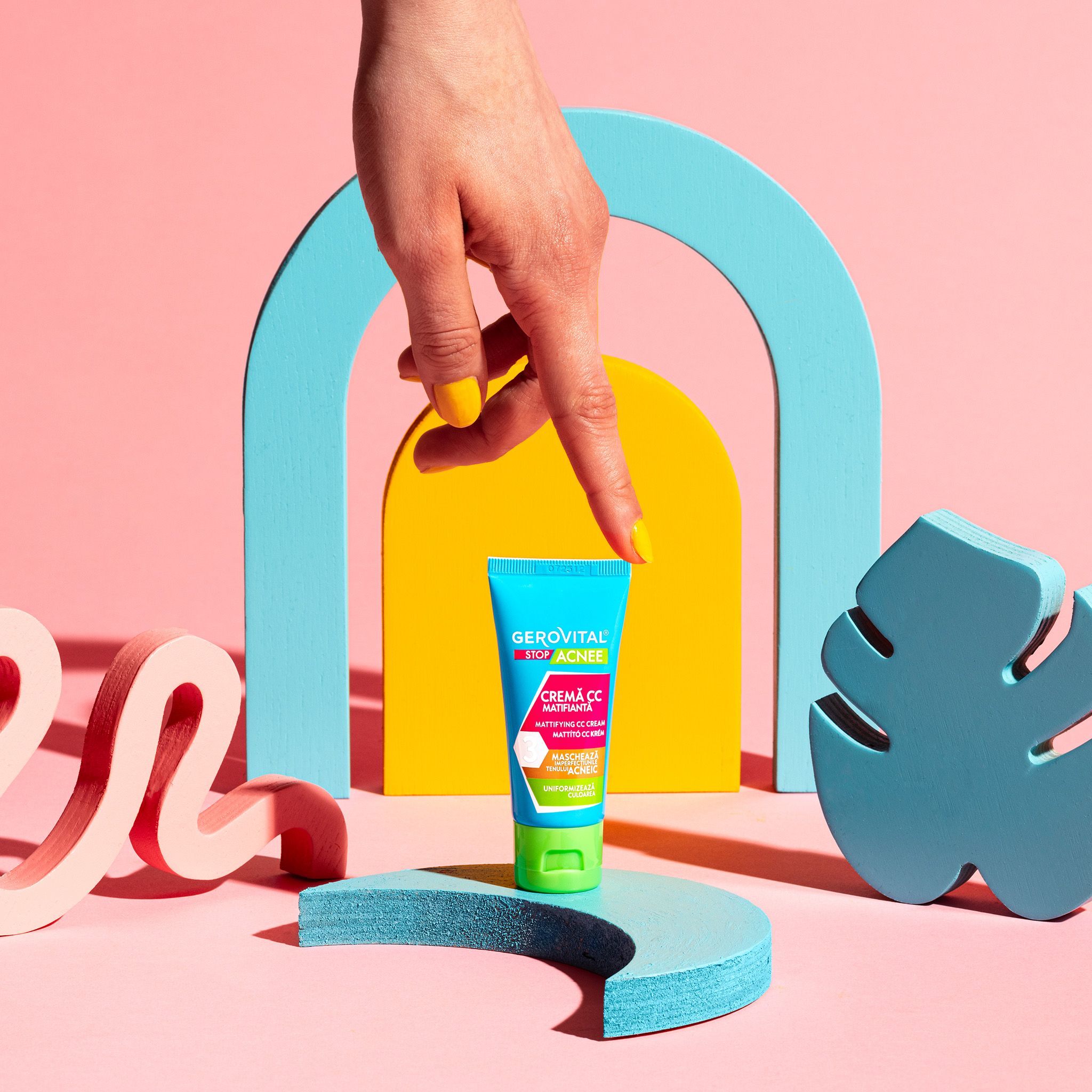 Tubo di crema CC Gerovital Stop Acnee su un piedistallo. Tubo turchese e verde con tappo verde. Mano gialla.