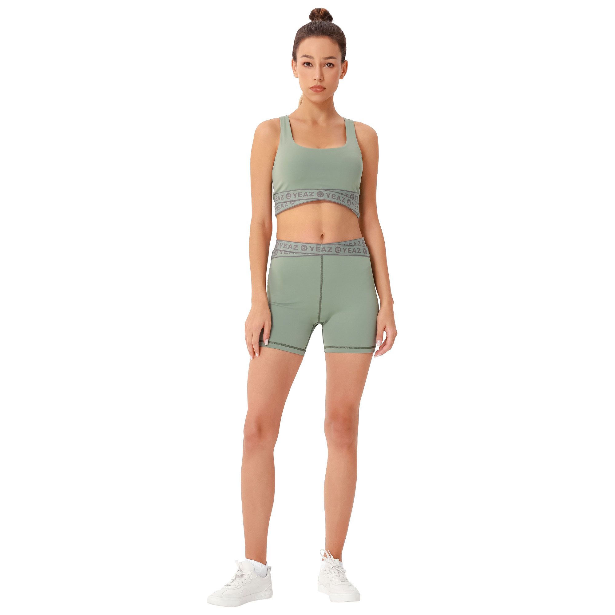 Reggiseno sportivo verde e pantaloncini da ciclista coordinati con dettaglio a fascia. Donna con sneakers bianche.