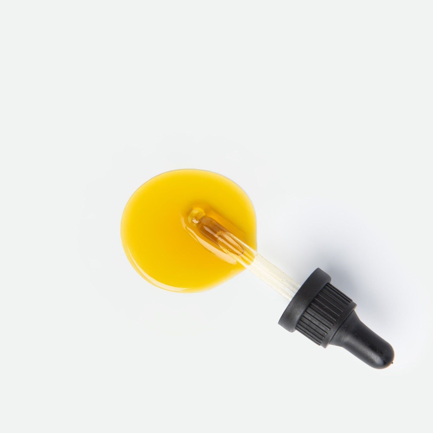 Goccia di olio giallo con pipetta di vetro e contagocce nero su sfondo bianco.