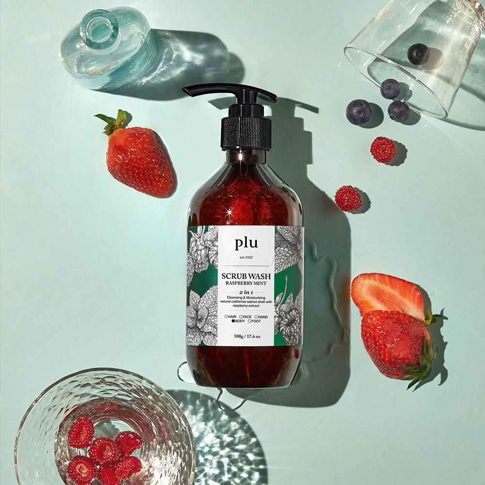 Flacone marrone con erogatore nero. Scritta: PLU Scrub Wash Raspberry Mint. Fragole, lamponi e mirtilli accanto.