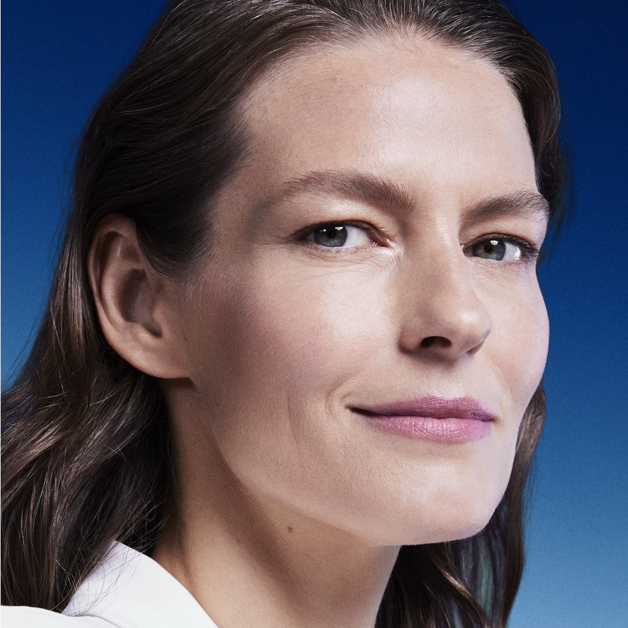 Ritratto di una donna con i capelli castani. Guarda la fotocamera e sorride leggermente. Sfondo blu.