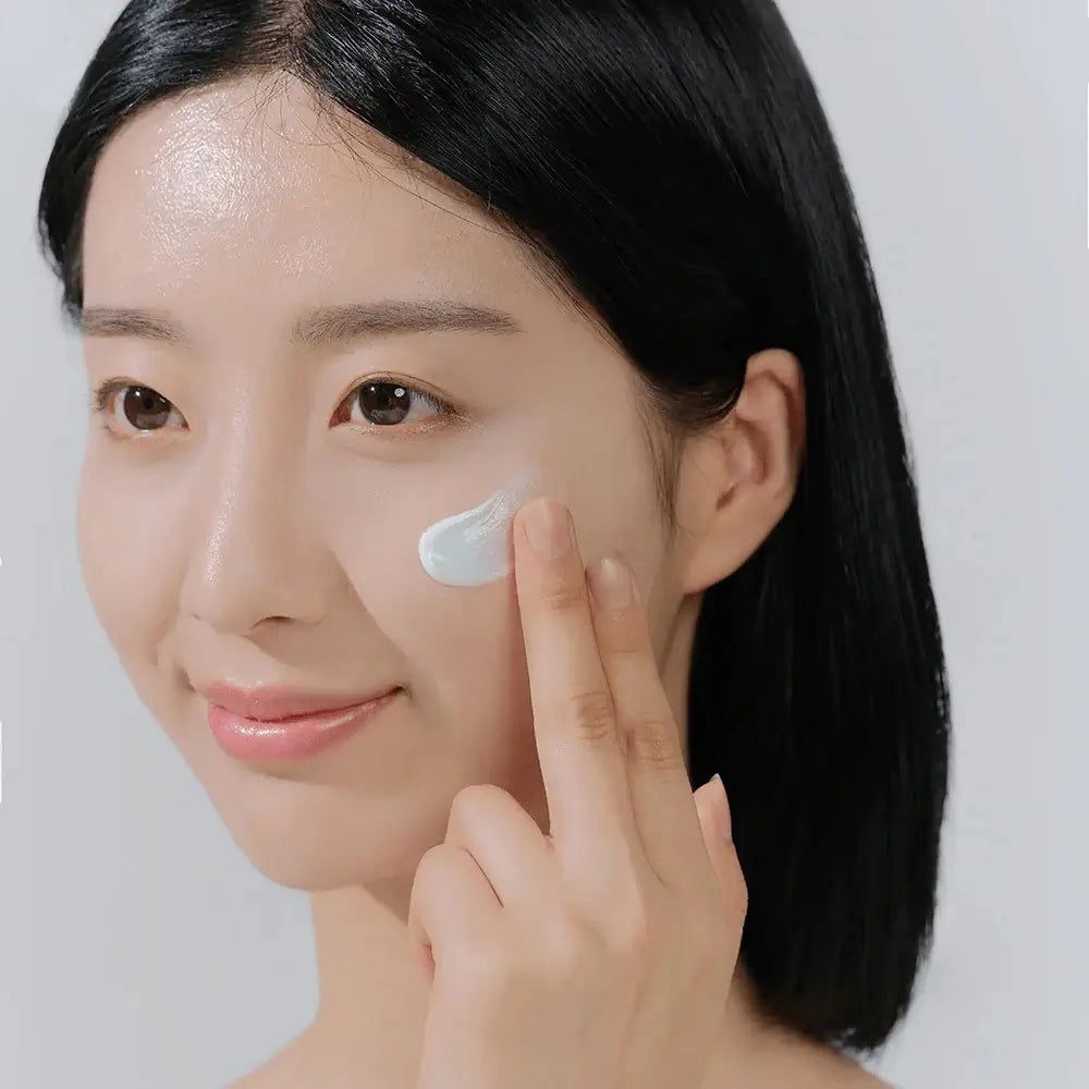 Donna applica crema sul viso. Crema chiara sulla pelle. Pelle chiara. Capelli neri.