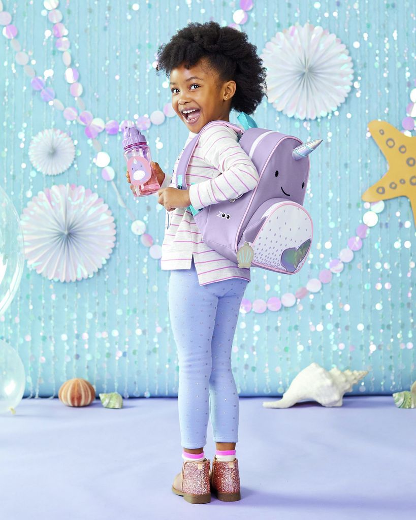 Bambina con zaino narvalo viola. La bambina indossa lo zaino e tiene una borraccia. Sfondo decorato.