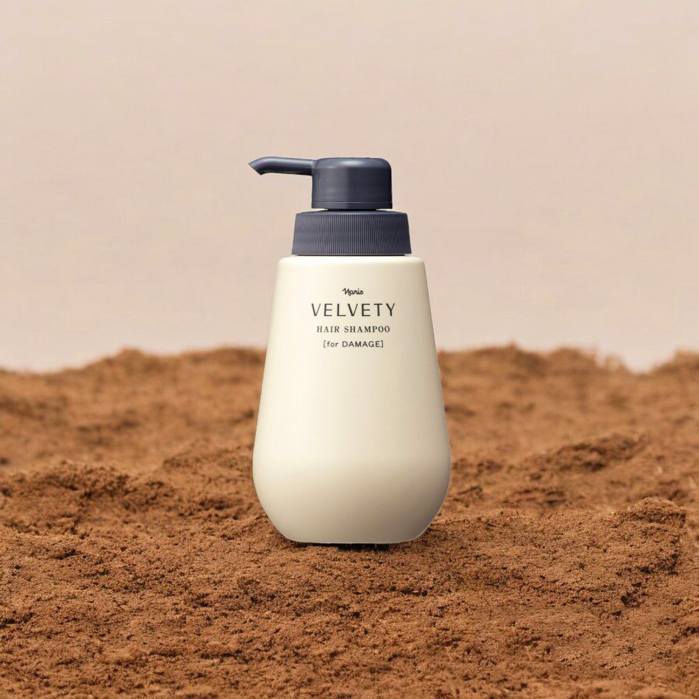 Flacone di shampoo VELVETY beige con dosatore grigio. Testo: HAIR SHAMPOO [for DAMAGE]. Su fondo marrone.