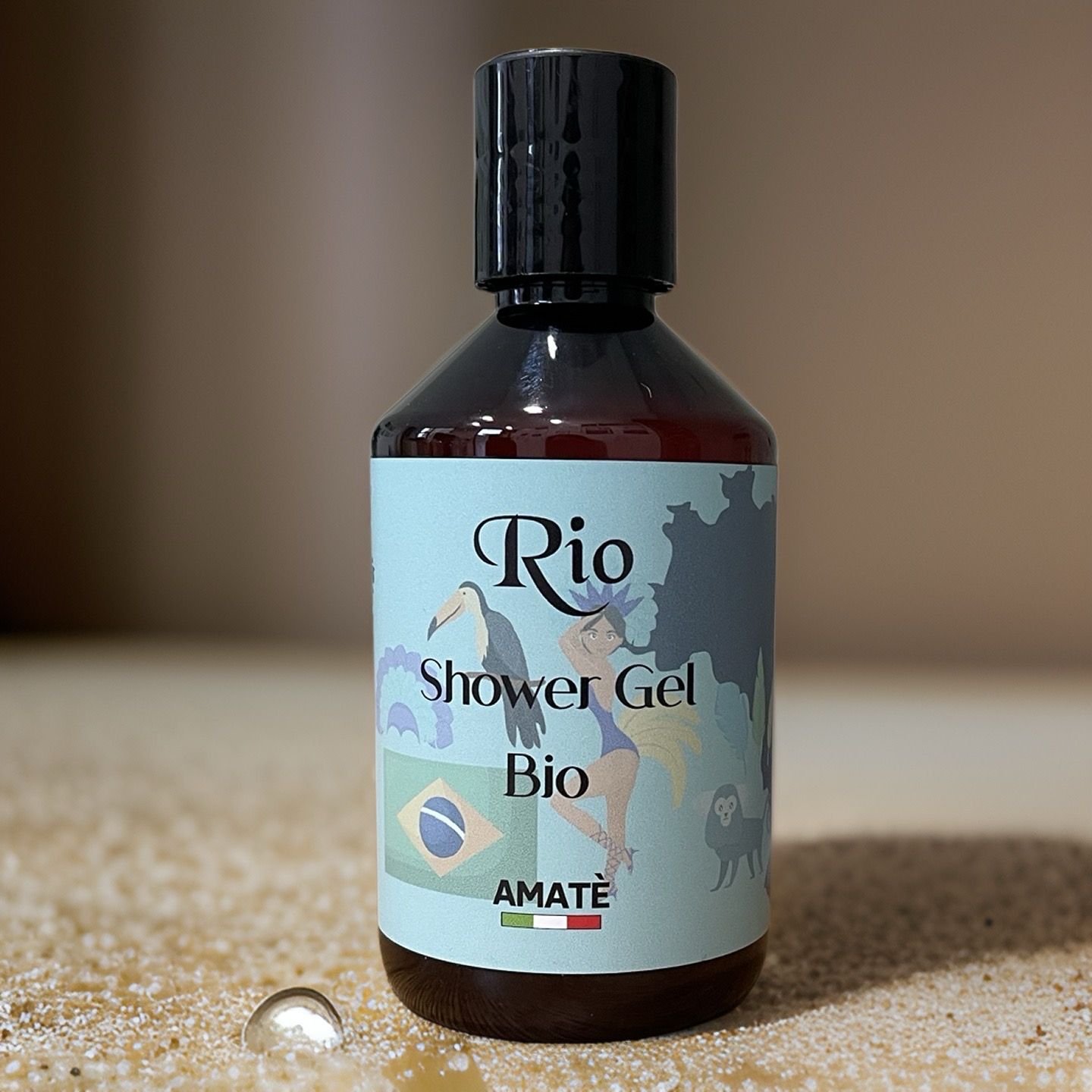Flacone marrone con tappo nero. Etichetta "Rio Shower Gel Bio" su sfondo sabbia. Marchio: AMATÈ.
