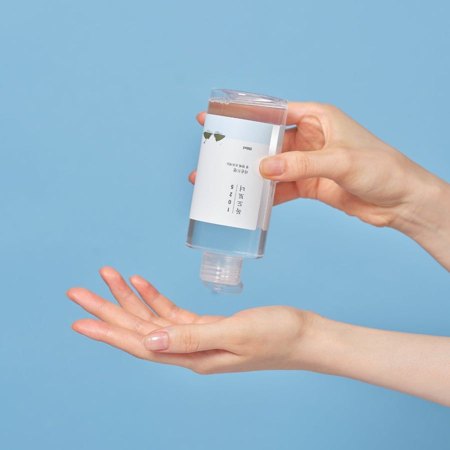 Flacone trasparente con etichetta bianca. Mani che tengono il flacone sopra un palmo. Sfondo blu.