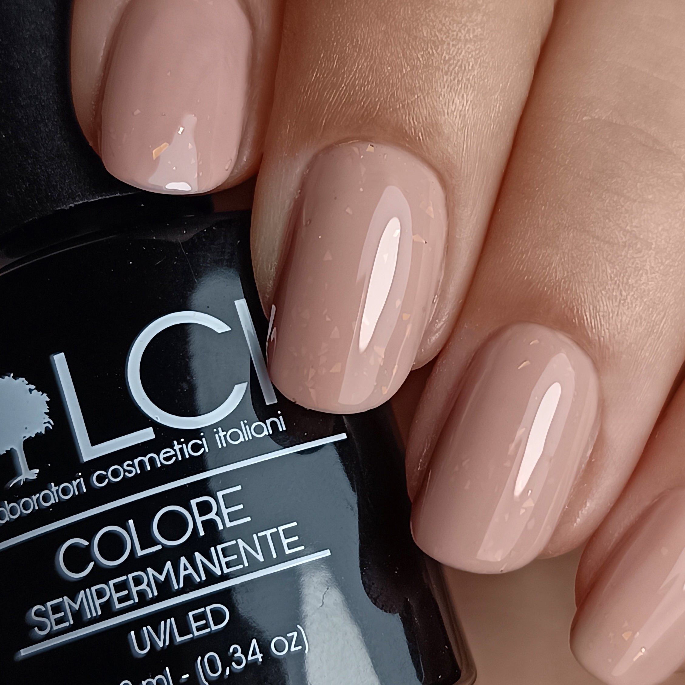 Mani con unghie smaltate beige. Sullo sfondo: flacone di smalto con scritta LCI, Colore Semipermanente.